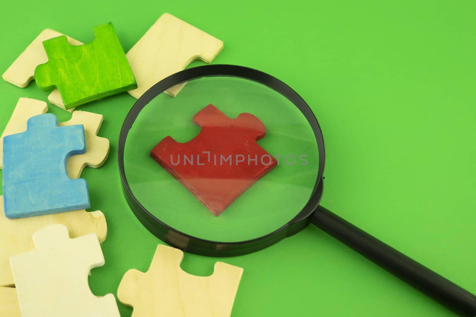 Selection of jigsaw puzzle pieces with magnifying glass on a green background with copy space conceptual of a search, teamwork and problem solving