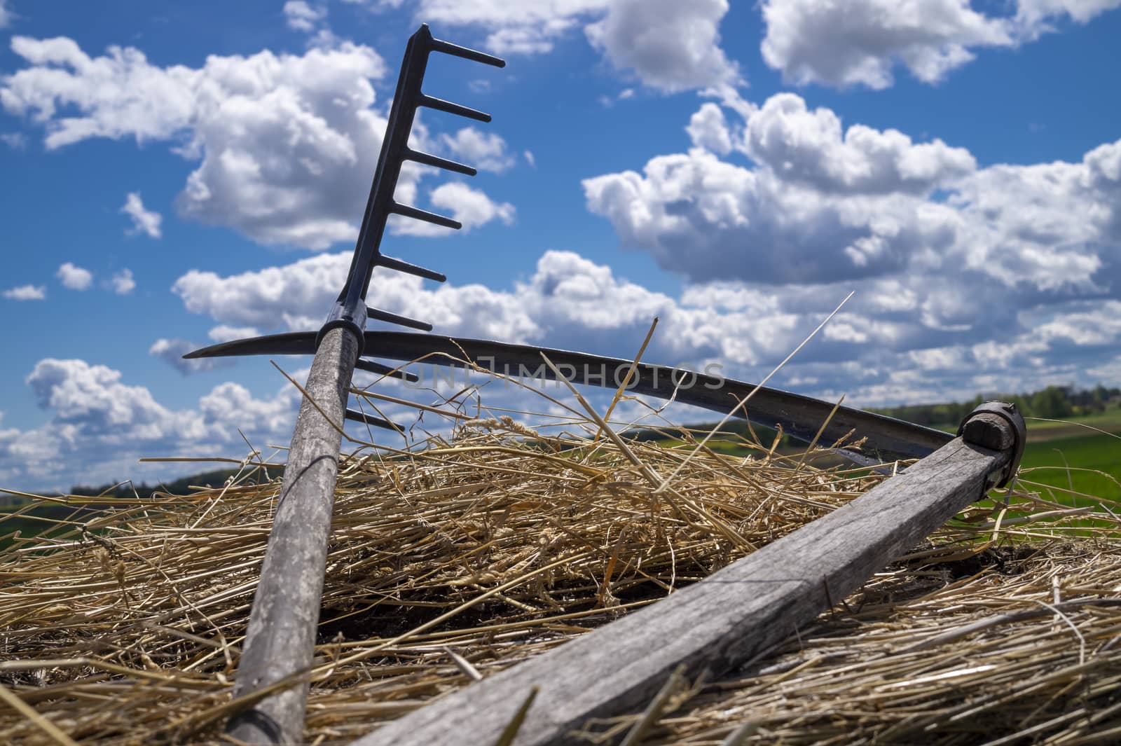 Rake and scythe on dried straw against a sunny blue sky with white clouds