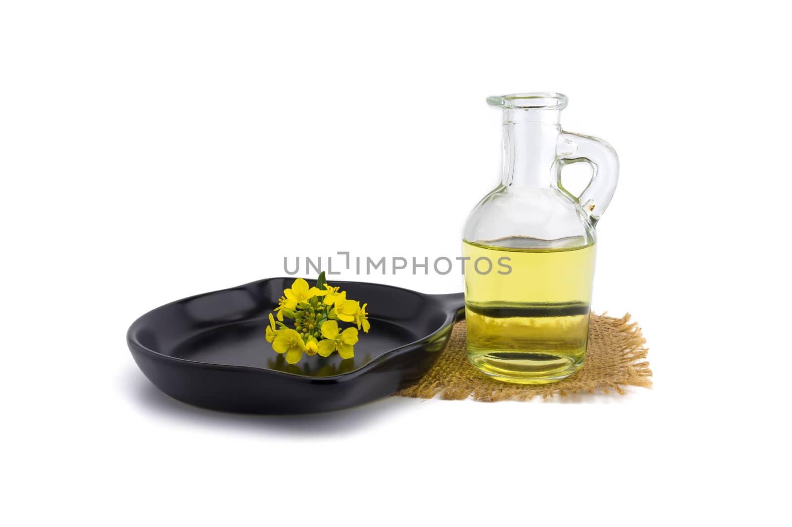 Small sprig of vivid yellow mustard or rapeseed flowers with decanter of oil on a cast iron skillet over a white background with copy space