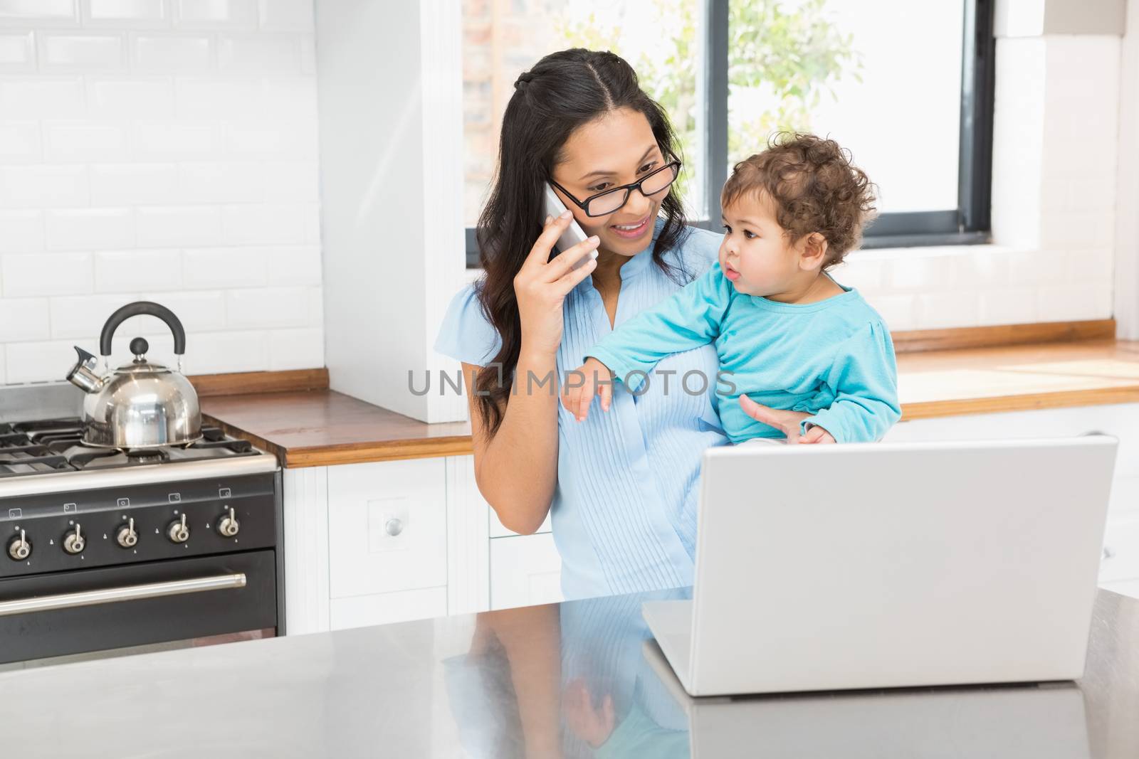 Smiling brunette holding her baby and using laptop on phone call by Wavebreakmedia