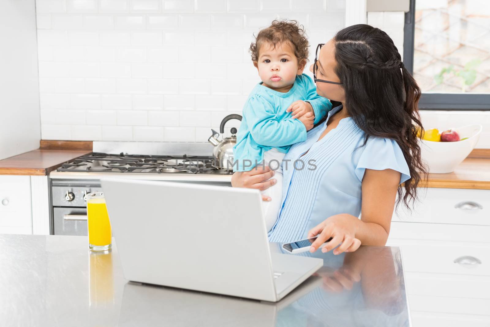 Smiling brunette holding her baby in the kitchen