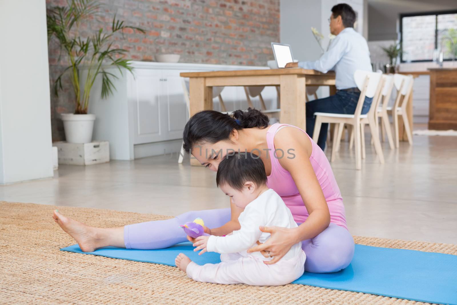 Happy mother and baby daughter sitting on exercising mat by Wavebreakmedia