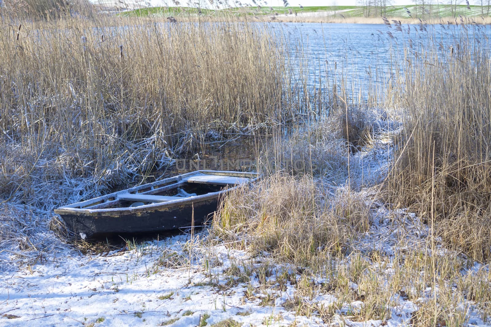 Old fishing boat among the reeds on the bank of a frozen river in winter, waiting on its time. Waiting for season concept