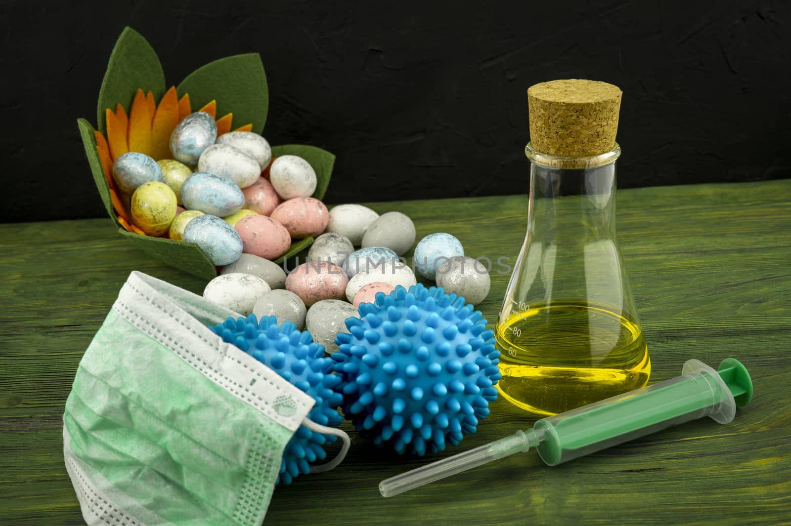 Virus pandemic and celebrating Easter concept with syringe and a protection mask, two blue virus molecules and glass container next to a Easter arrangement with traditional painted eggs