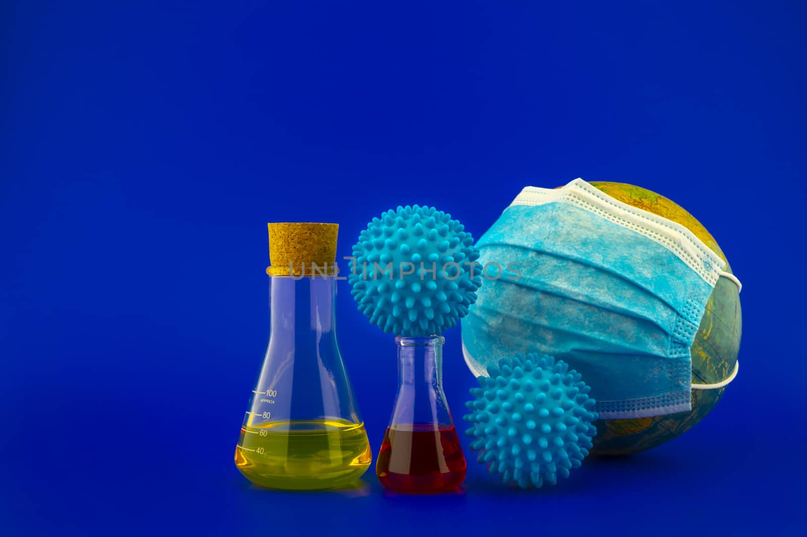 Concept of research for a Covid-19 vaccine with a conical lab flasks with yellow and red solutions alongside a hypodermic syringe and blue virus molecules over a blue background with copy space