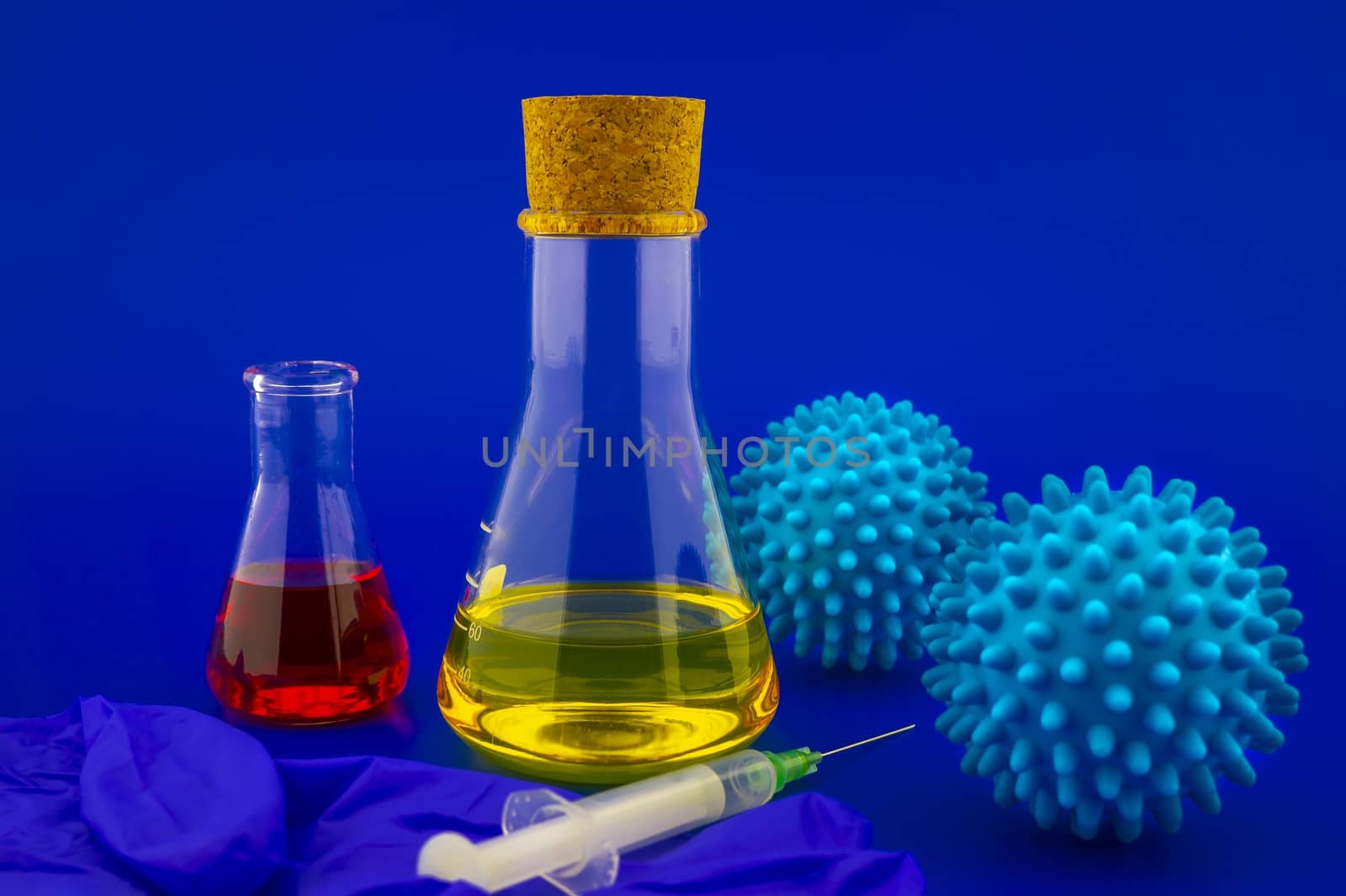 Concept of research for a Covid-19 vaccine with a conical lab flasks with yellow and red solutions alongside a hypodermic syringe and blue virus molecules over a blue background with copy space