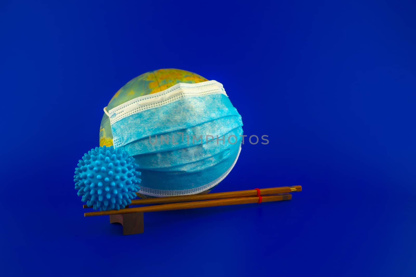 Virus pandemic concept concept with two blue virus molecule balanced on chopsticks with a surgical mask around world globe behind over a blue background