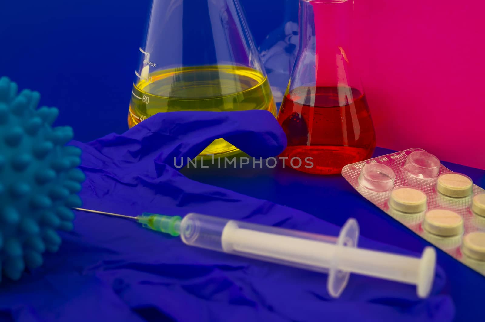 Concept of research for a virus vaccine with a conical lab flasks with yellow and red solutions alongside a hypodermic syringe and blue virus molecules with blank square of paper note for text