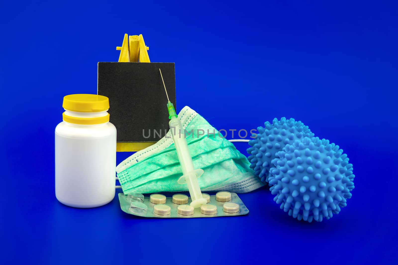 Virus pandemic and possible vaccine concept with surgical mask, hypodermic syringe, pharmaceutical bottle small chalk board and blue virus molecules in blue toned theme with with copy space