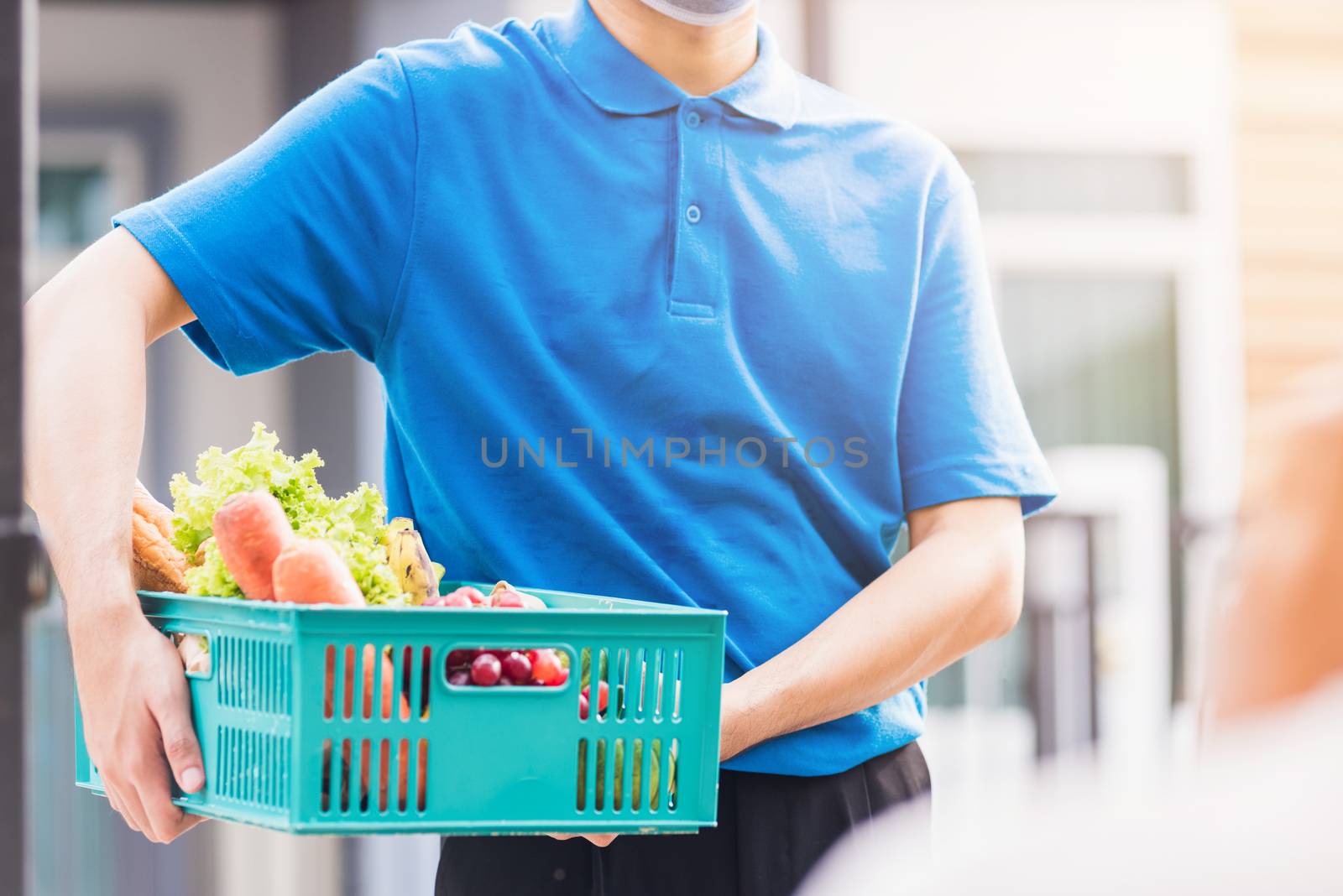 Asian grocery store delivery man wearing blue uniform and face mask protect he delivering fresh food vegetable in plastic box at door front home after coronavirus outbreak, back to new normal concept