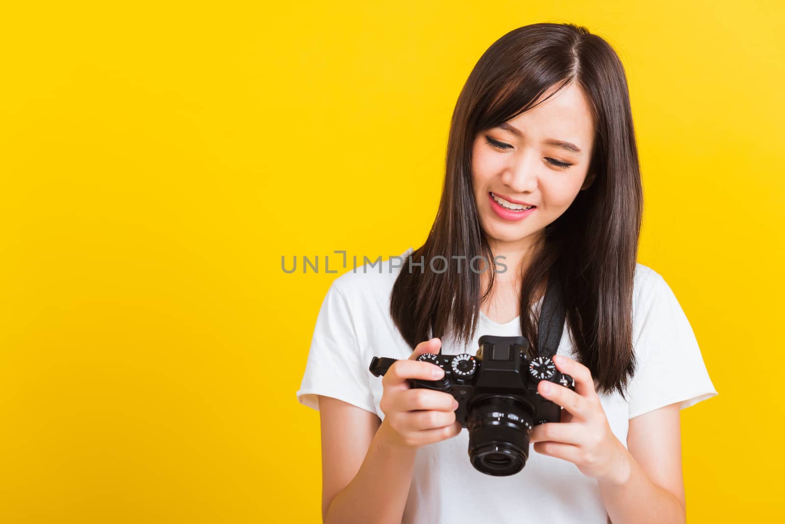 Portrait of happy Asian beautiful young woman photographer review picture she seeing a photo on the screen of digital mirrorless photo camera after photography, isolated on yellow background