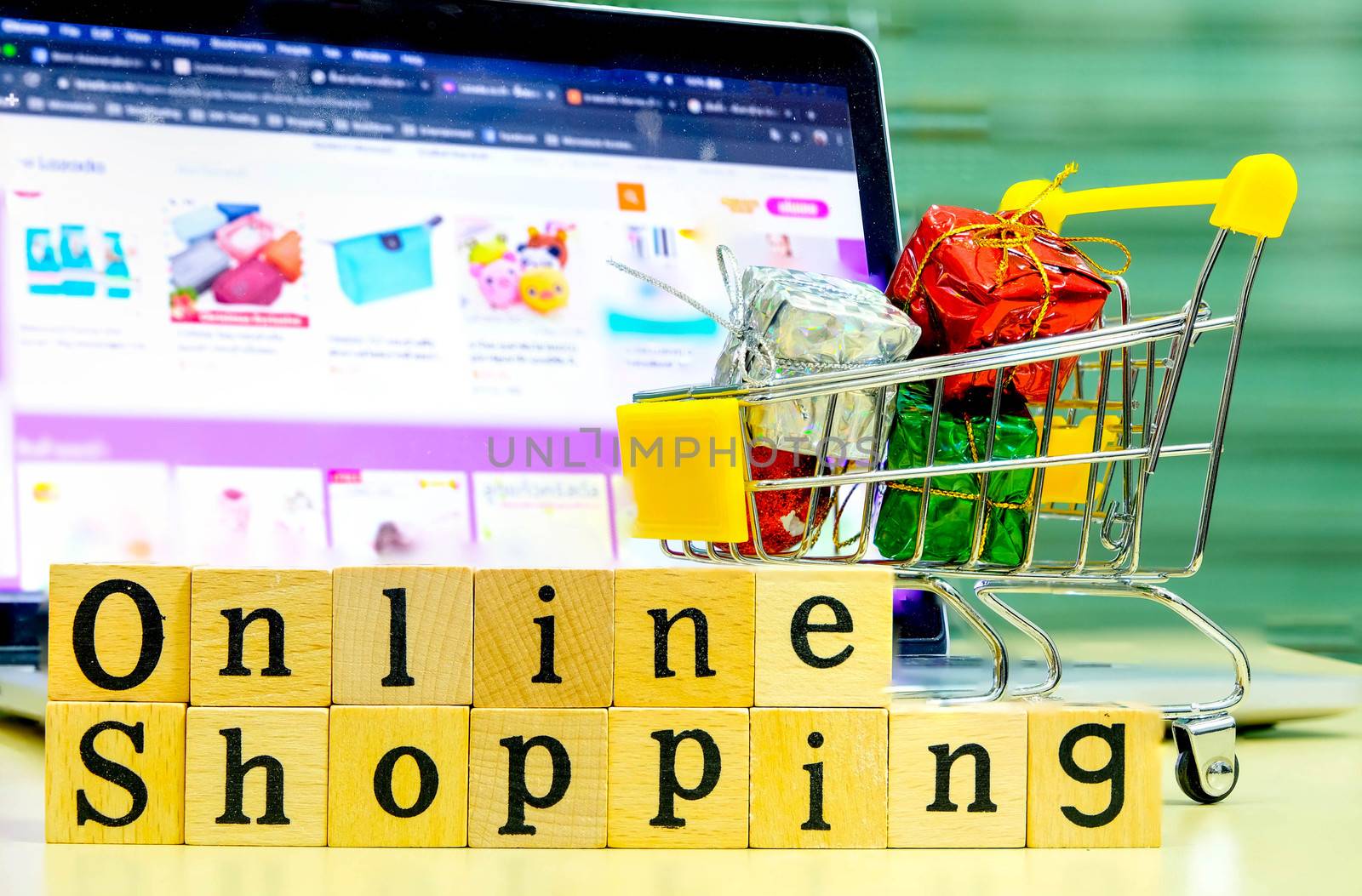Wooden Alphabet "online shopping" and shopping cart with full of presents or gifts in front of the Blur Shopping Online Website on Laptop