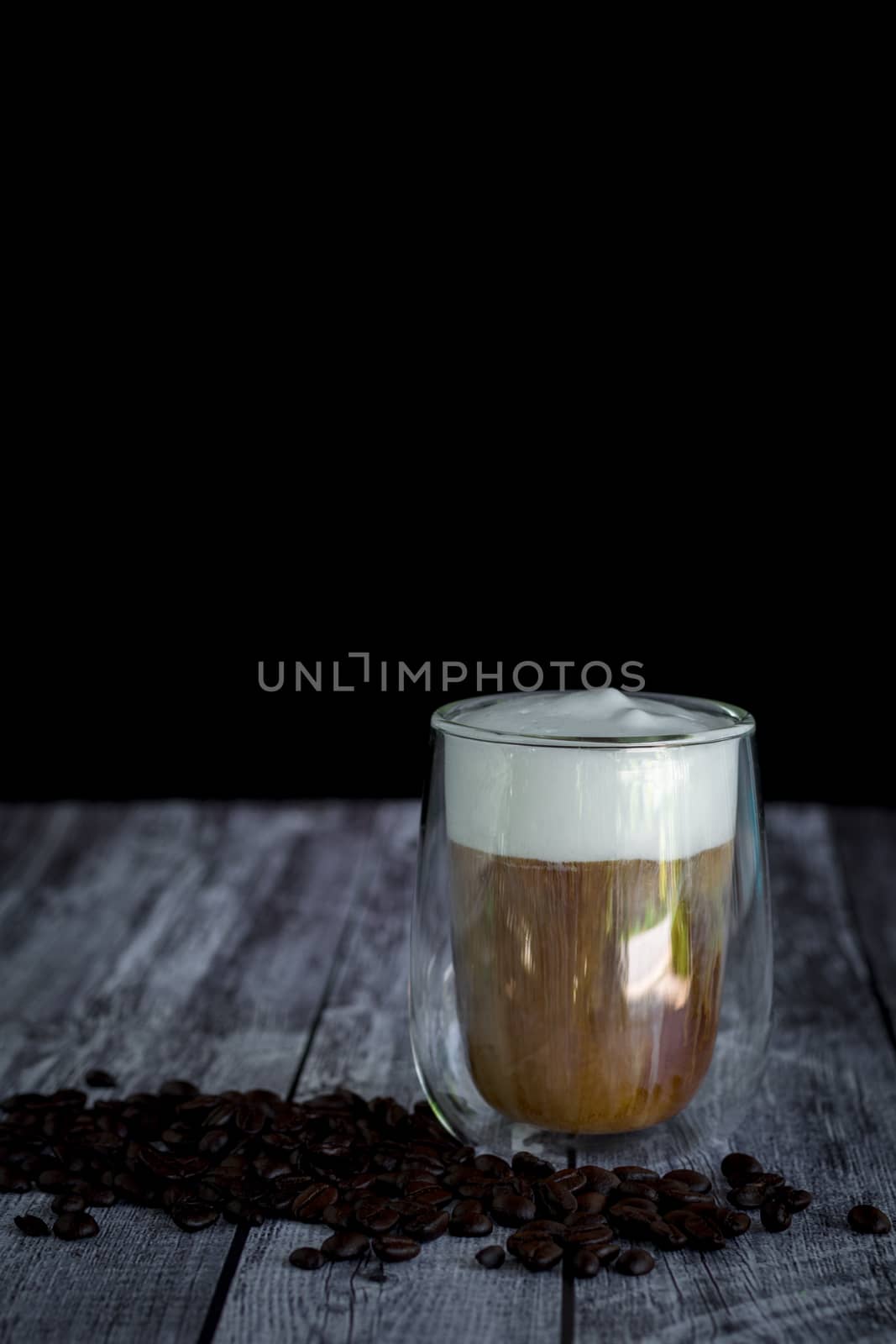 Coffee time and refreshment concept. Transparent glass of coffee with milk froth and roasted coffee bean on wooden background.