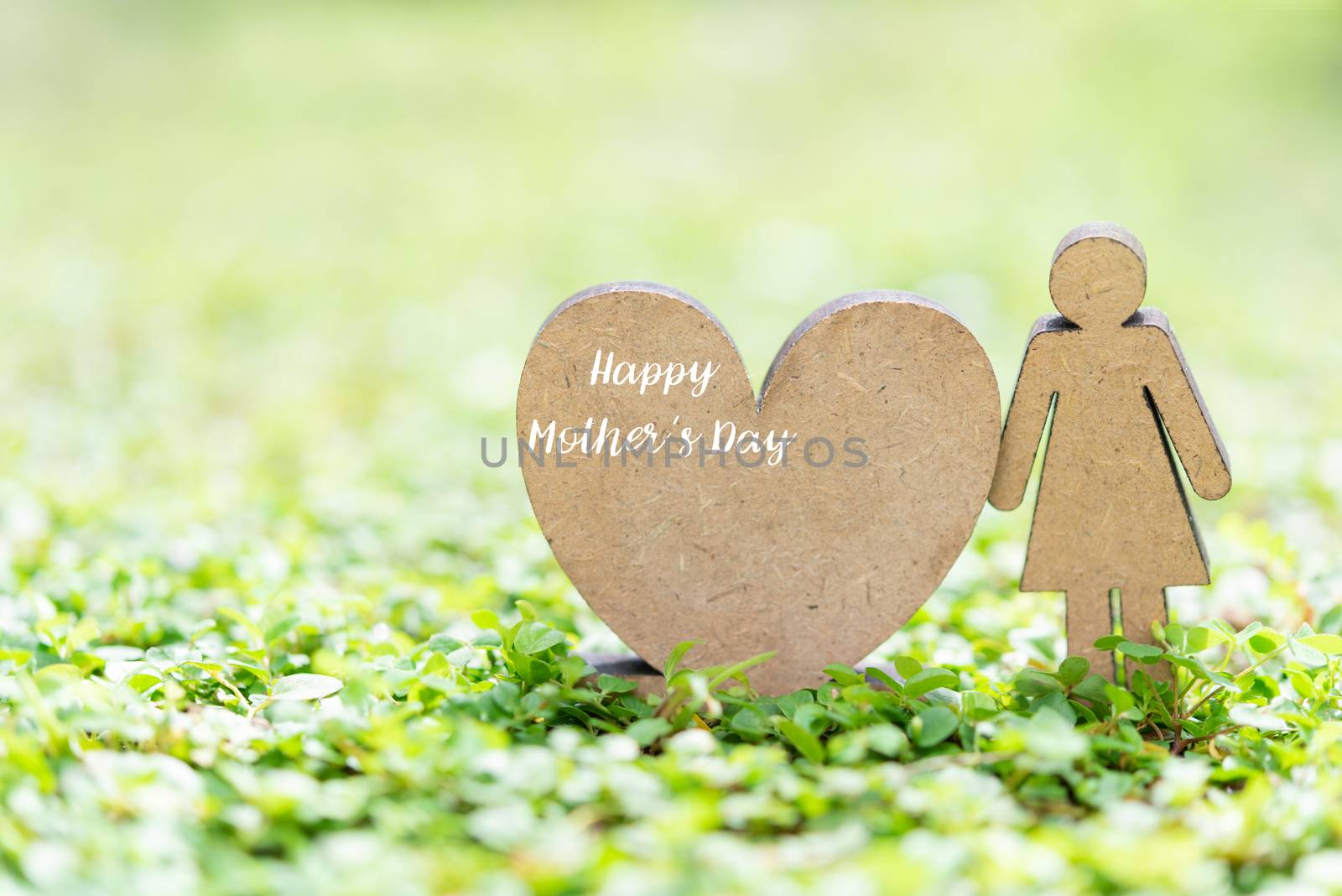 Happy Mother’s Day with heart icon and woman model stand on fresh green grass in garden with copy space for text