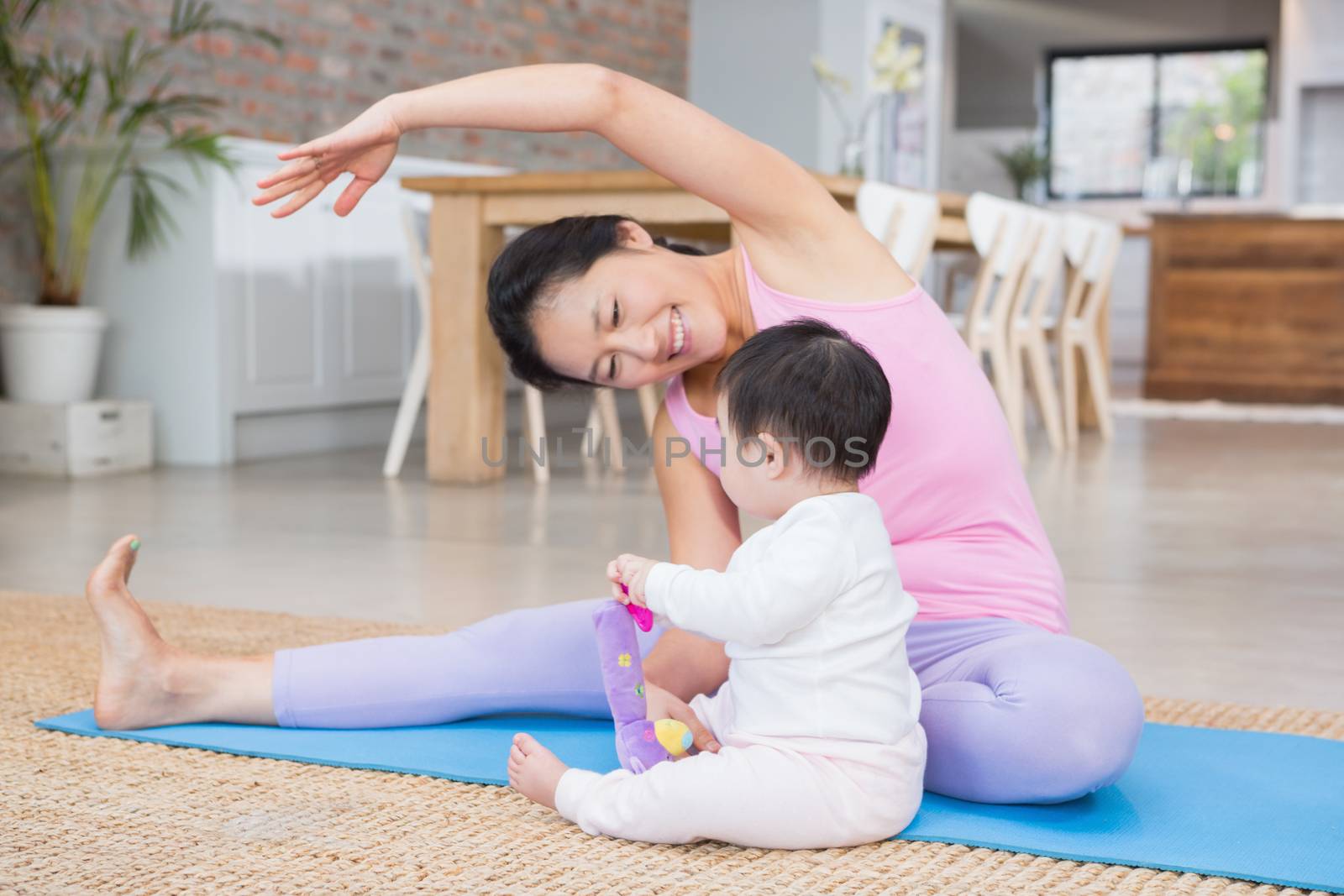 Happy mother doing yoga on mat while looking at baby daughter by Wavebreakmedia