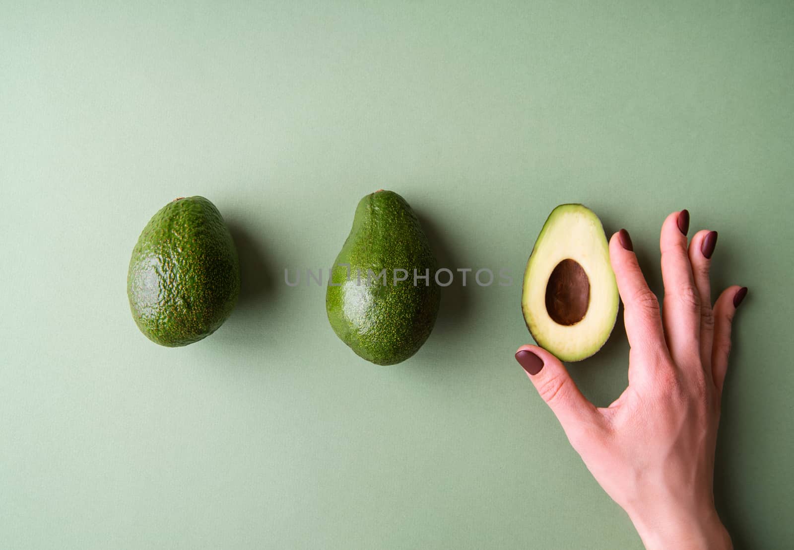 Healthy food concept. Woman hand holding a half of avocado on the green background top view