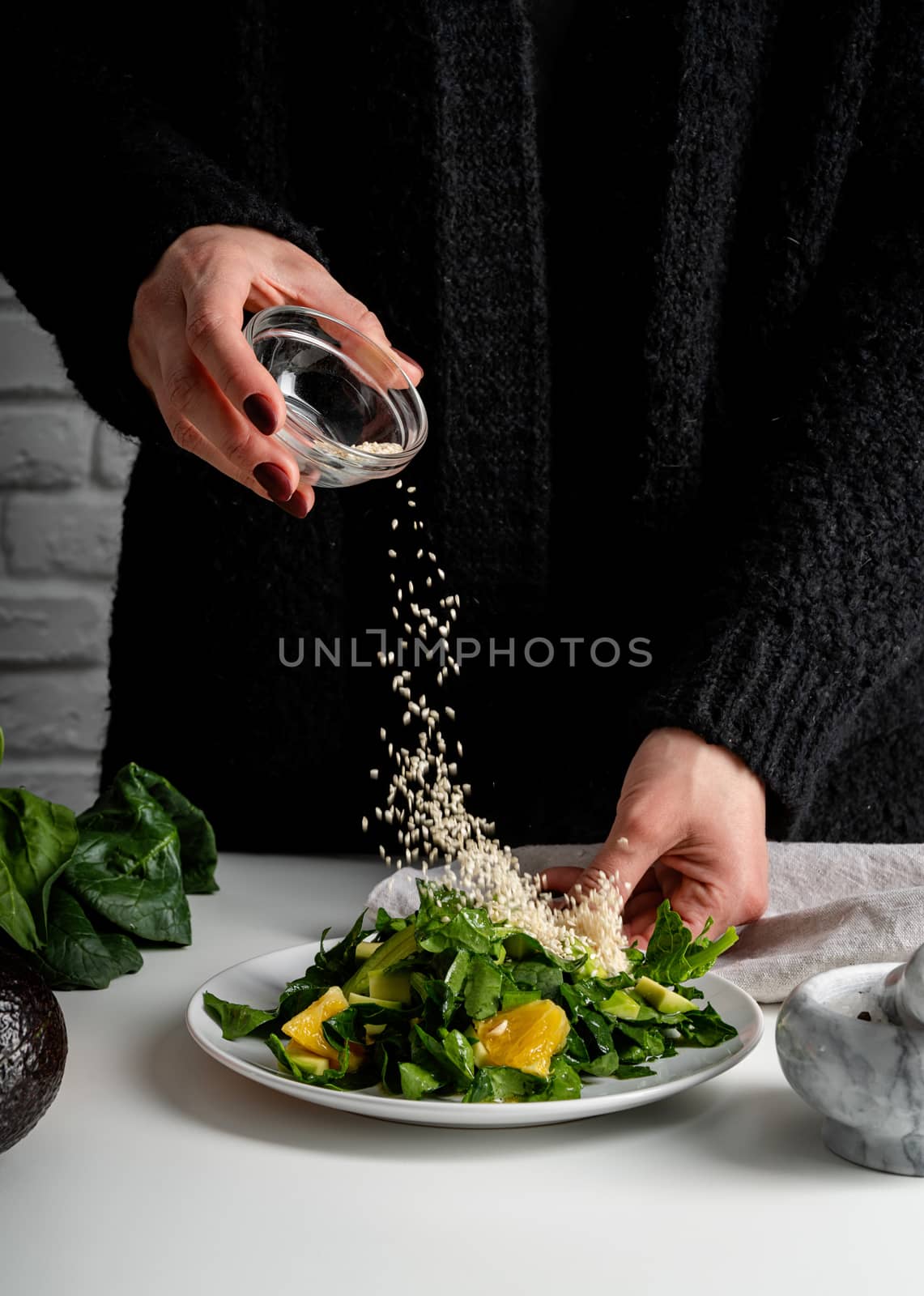 Step by step preparation of spinach, avocado and orange salad. Step 8 - pouring sesame seeds for decoration, front view, selective focus