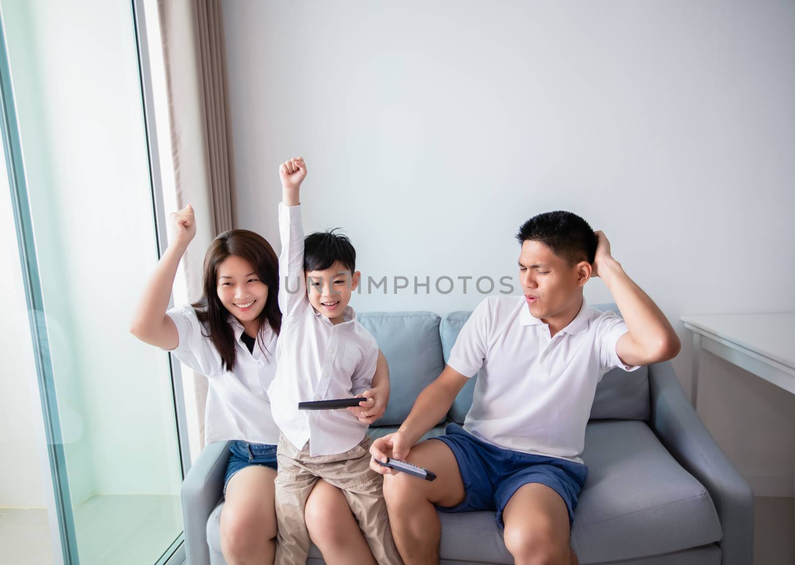 Asian family having fun playing computer console games together, Father and son have the handset controllers and the mother is cheering the players at home