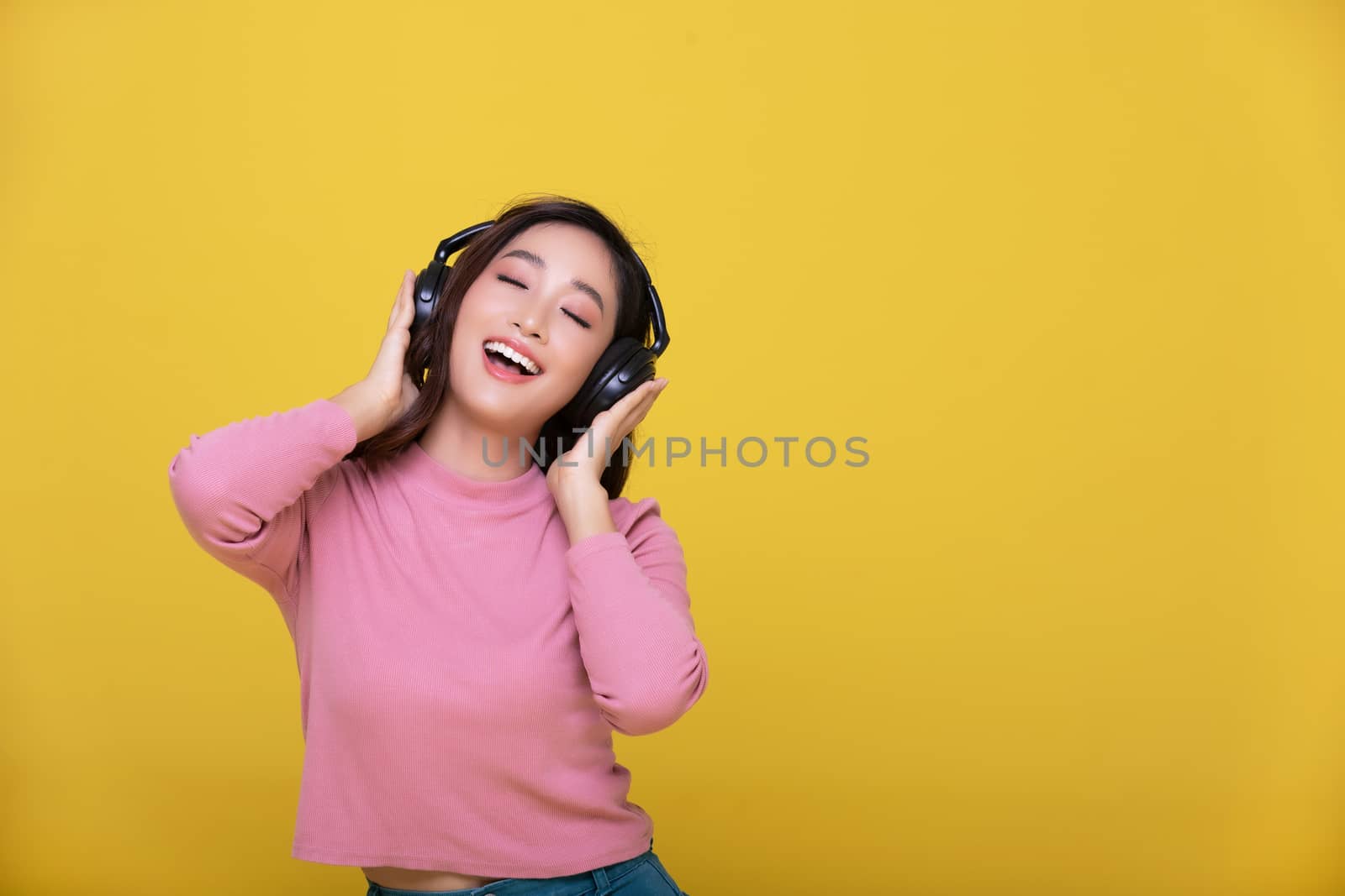 Happy cheerful Beautiful Asian woman wearing wireless headphones enjoying listening to music on yellow background.People lifestyle concept