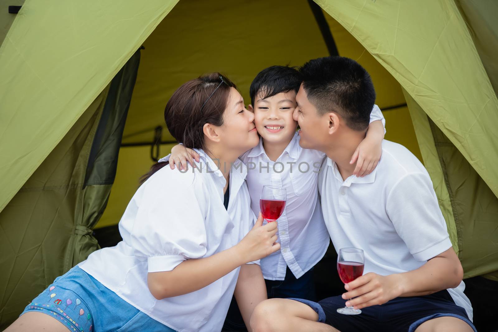 Asian family smiles, laughs and enjoys camping and picnic at the beach with tent on a summer vacation.