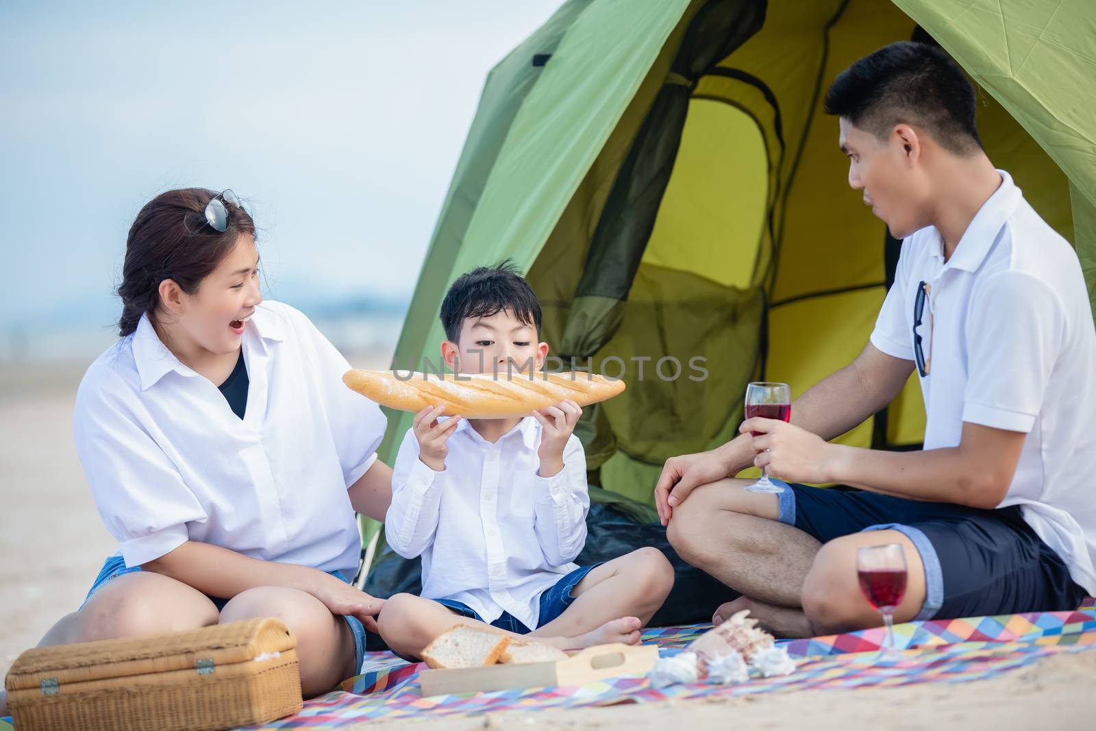 Asian family smiles, laughs and enjoys camping and picnic at the beach with tent on a summer vacation.