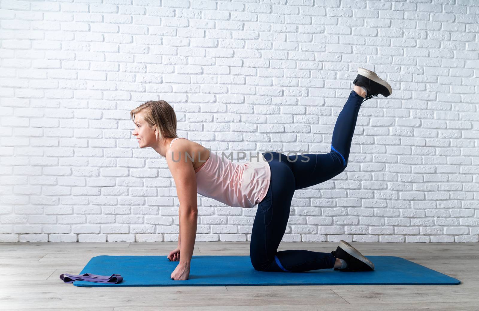 Stay home. Home fitness. Smiling young sportswoman doing the exercises on all fours arching back straightening leg up indoors
