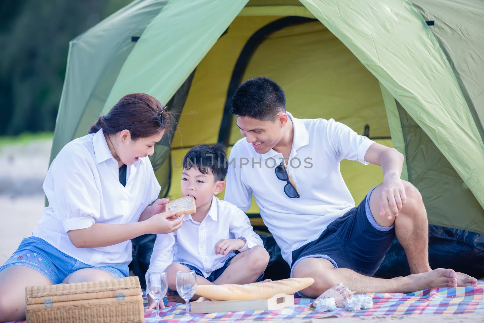 Asian family smiles, laughs and enjoys camping and picnic at the beach with tent on a summer vacation.