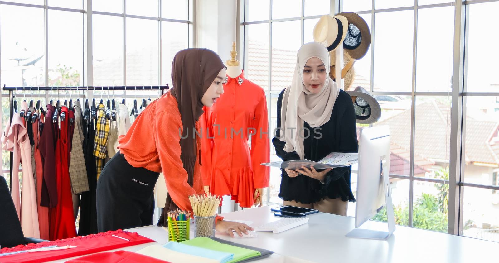 Small business of Muslim woman fashion designer Working and  using smart phone and tablet With Dresses at clothing store by Tuiphotoengineer