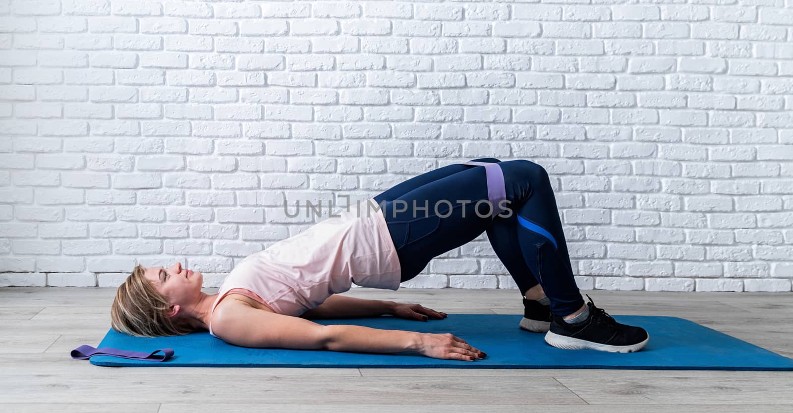 Stay home. Home fitness. Woman doing exercise for glute hip bridge abduction using rubber resistance band