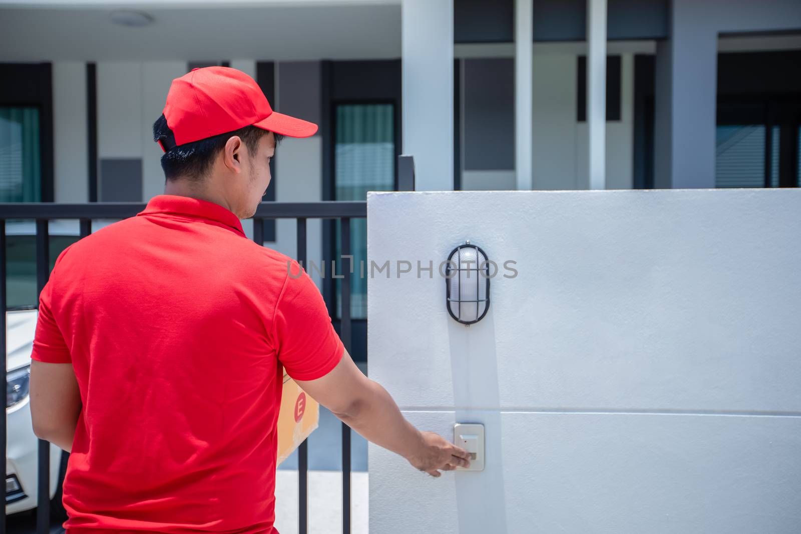 Asian delivery servicemen wearing a red uniform with a red cap handling cardboard boxes to give to the customer in front of the house and Click the doorbell. Online shopping and Express delivery