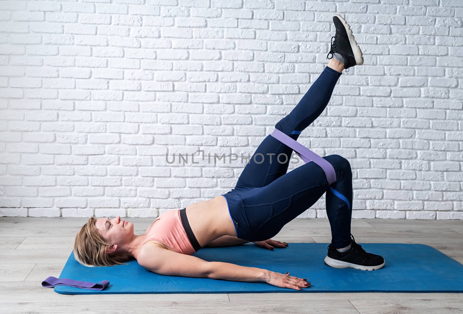 Woman doing exercise for glute hip bridge with a leg up abduction using rubber resistance band by Desperada