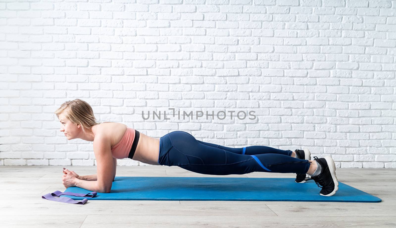 Stay home. Home fitness. Young blond woman doing plank at home, white brick wall and wooden floor