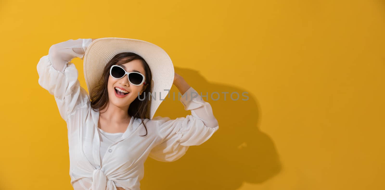 Portrait Asian beautiful happy young woman with sunglasses and hat smiling cheerful in summer and looking at camera isolated on yellow studio background.