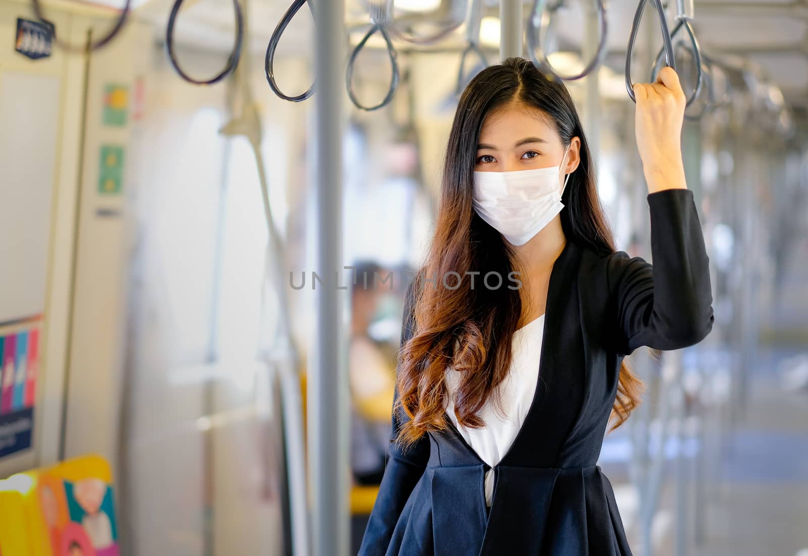 Portrait of beautiful business woman with hygiene mask stand with hold handrail in sky train by nrradmin