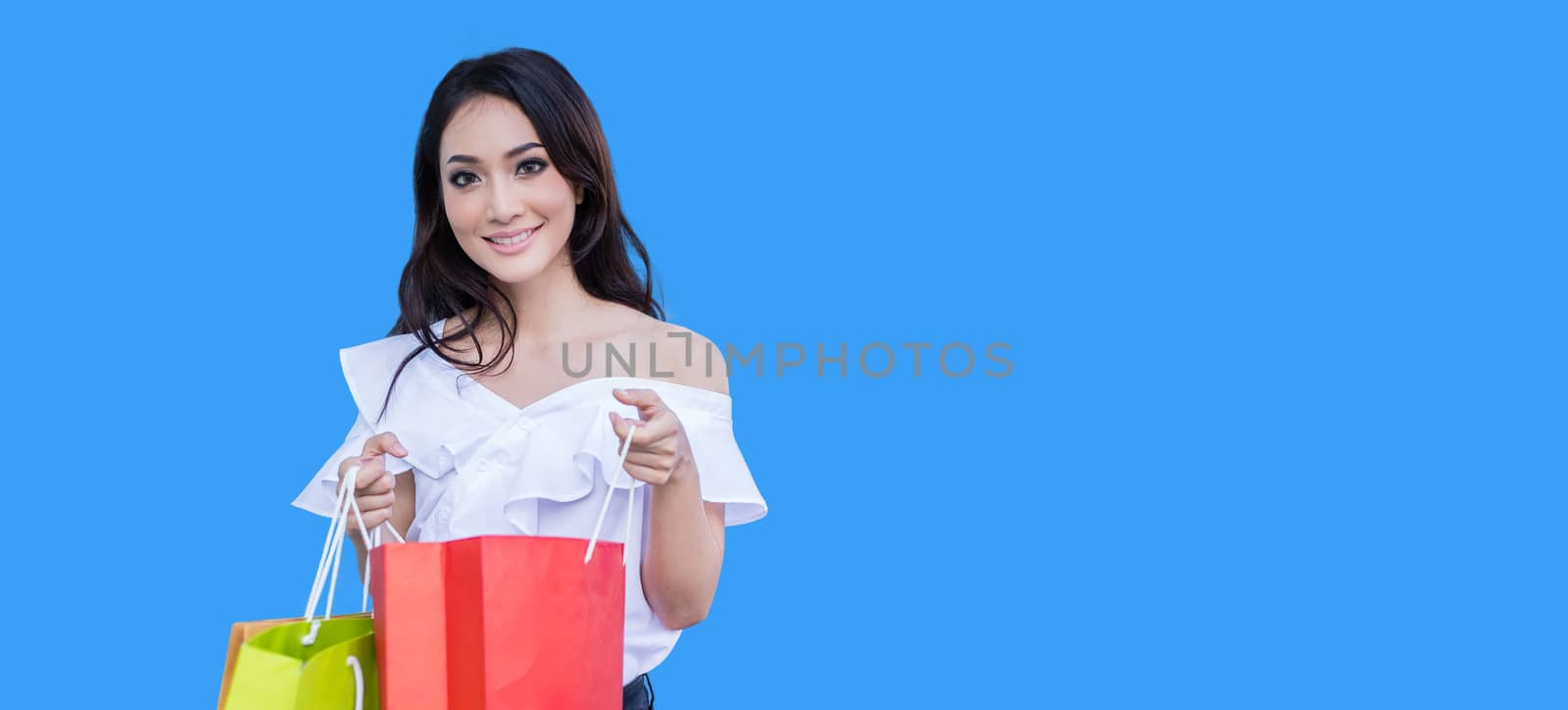 Beautiful asian young woman is standing holding shopping bags .She smile happiness in the shopping mall on blue background