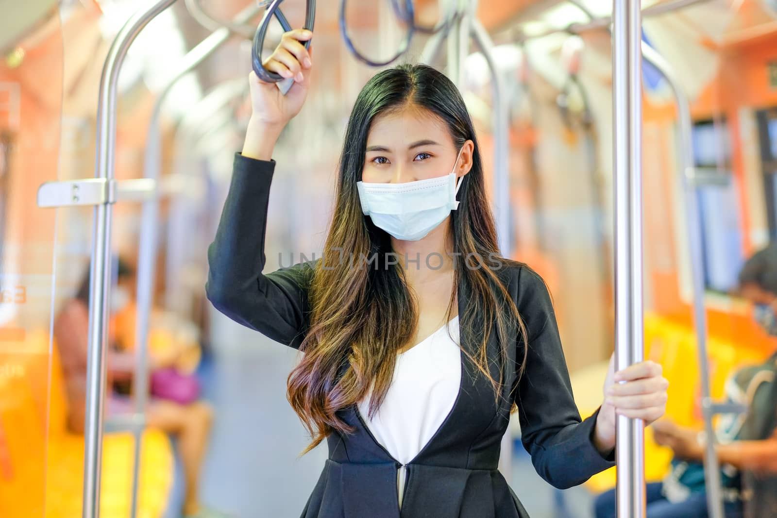 Portrait of beautiful business woman with hygiene mask stand with hold handrail and pole in sky train along the way for working during coronavirus spreading in city.