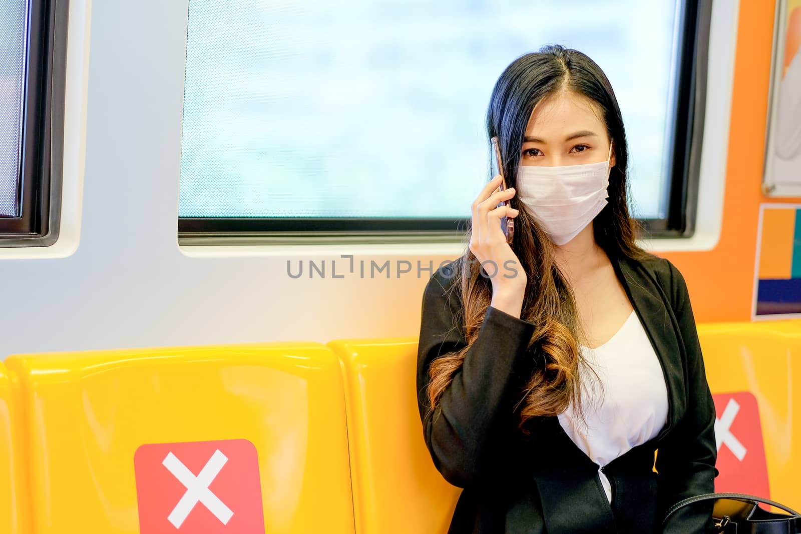 Portrait of beautiful business woman with hygiene mask use mobile phone and sit on separated seat in sky train during go to work on coronavirus spreading in city.