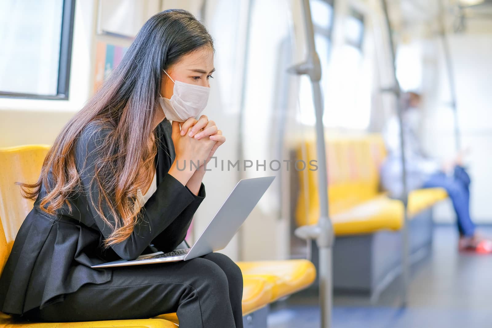 Beautiful business girl with hygiene mask sit with laptop and action of seriously thinking about her work in sky train during Covid-19 coronavirus pandemic in city.
