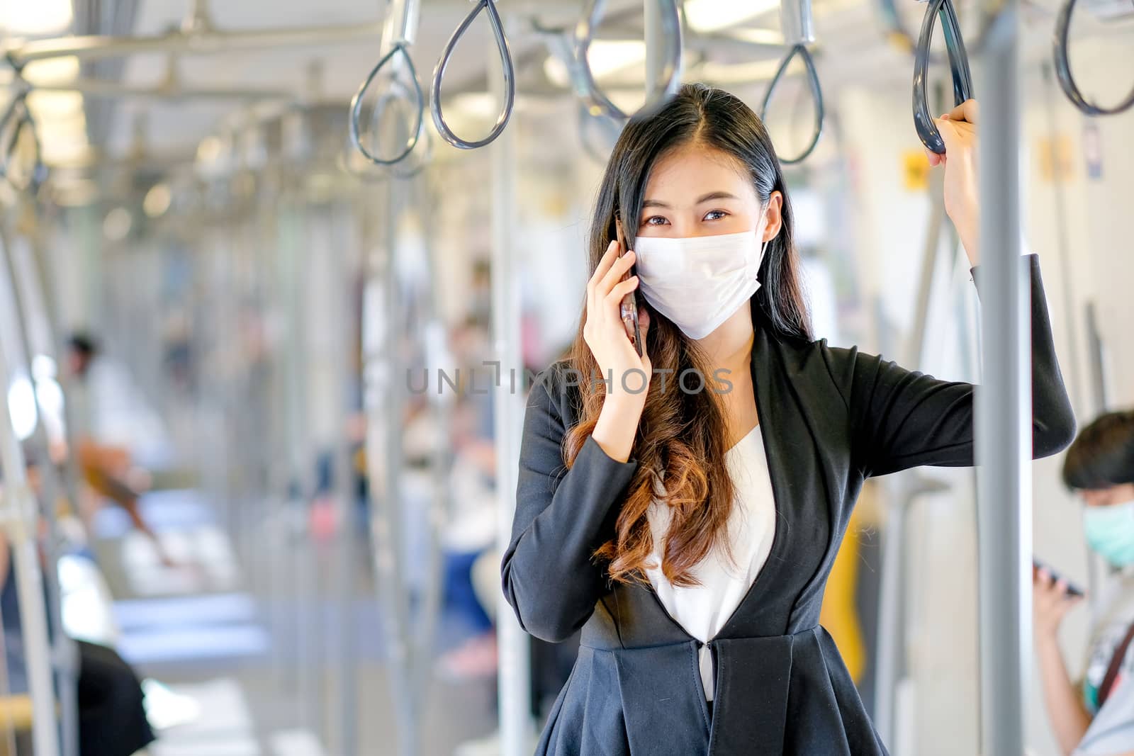 Portrait of beautiful business woman with hygiene mask use mobile phone and stand with hold handrail in sky train by nrradmin