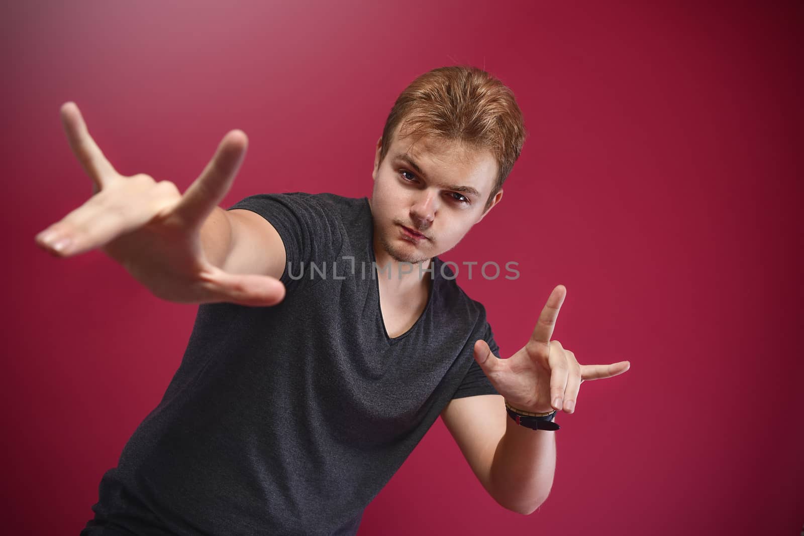 Young pathos Teenager boy wearing grey t-shirt over isolated pink background doing rock symbol with hands up. Music star. yo sign. cool sign