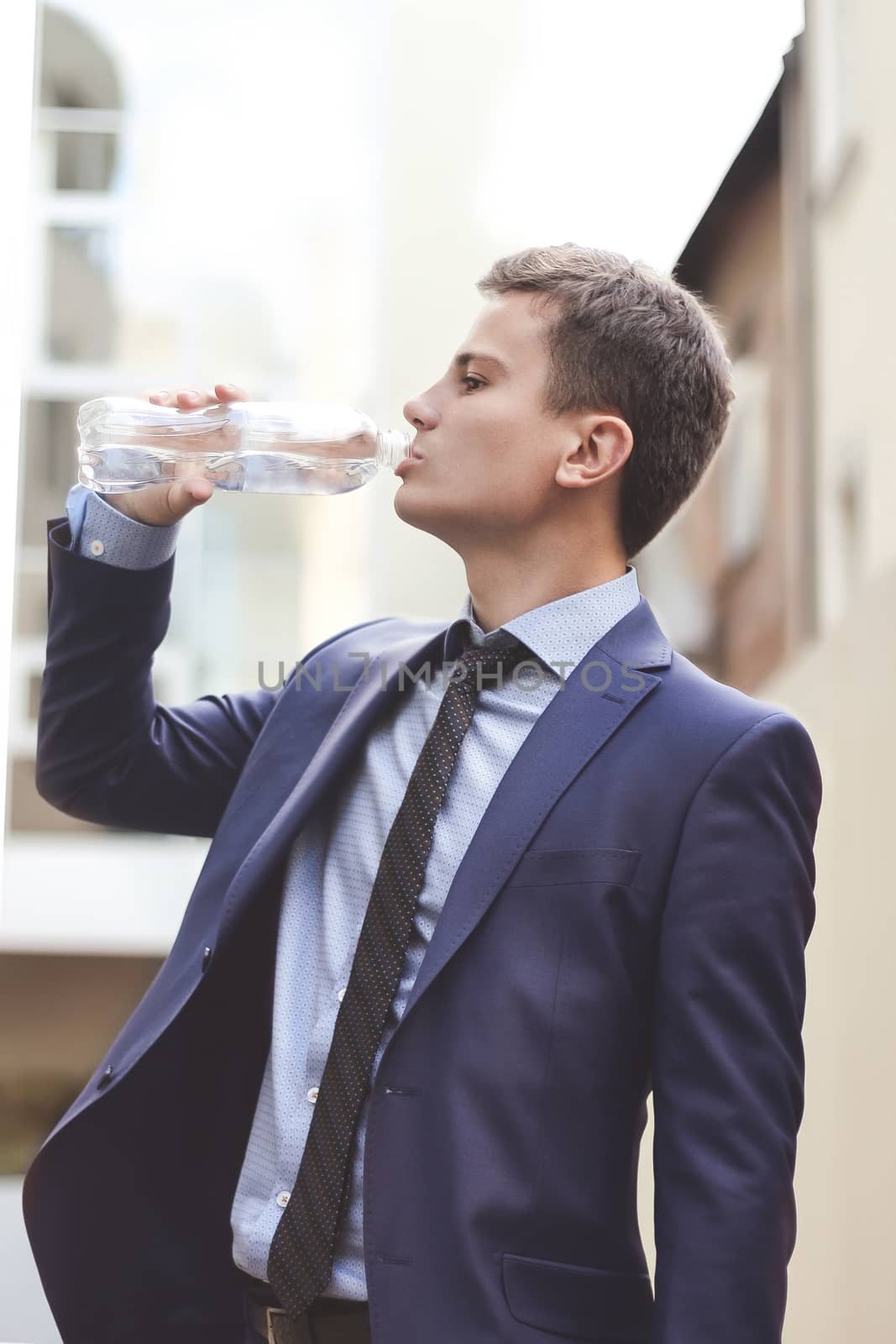 Business man with suit holding water bottle and drinking outdoor. The young Business man drink fresh water