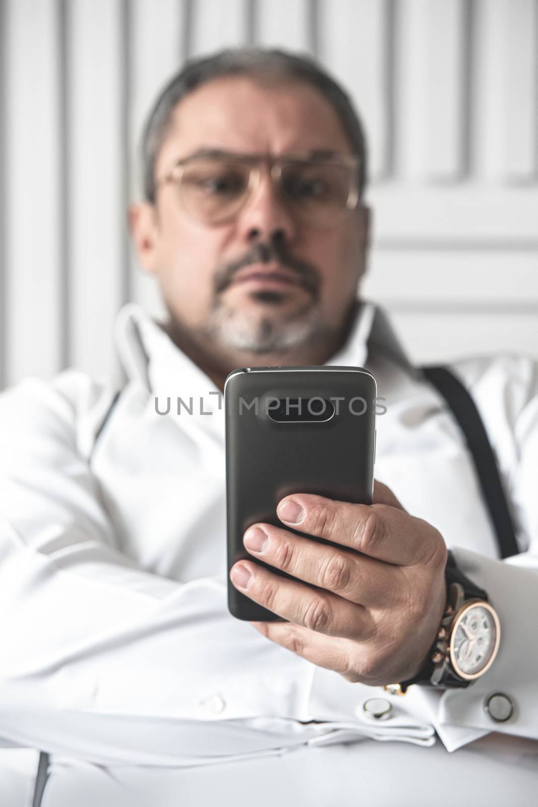 The bad news. A seriously displeased businessman in a white shirt is looking on the phone. foreground focus