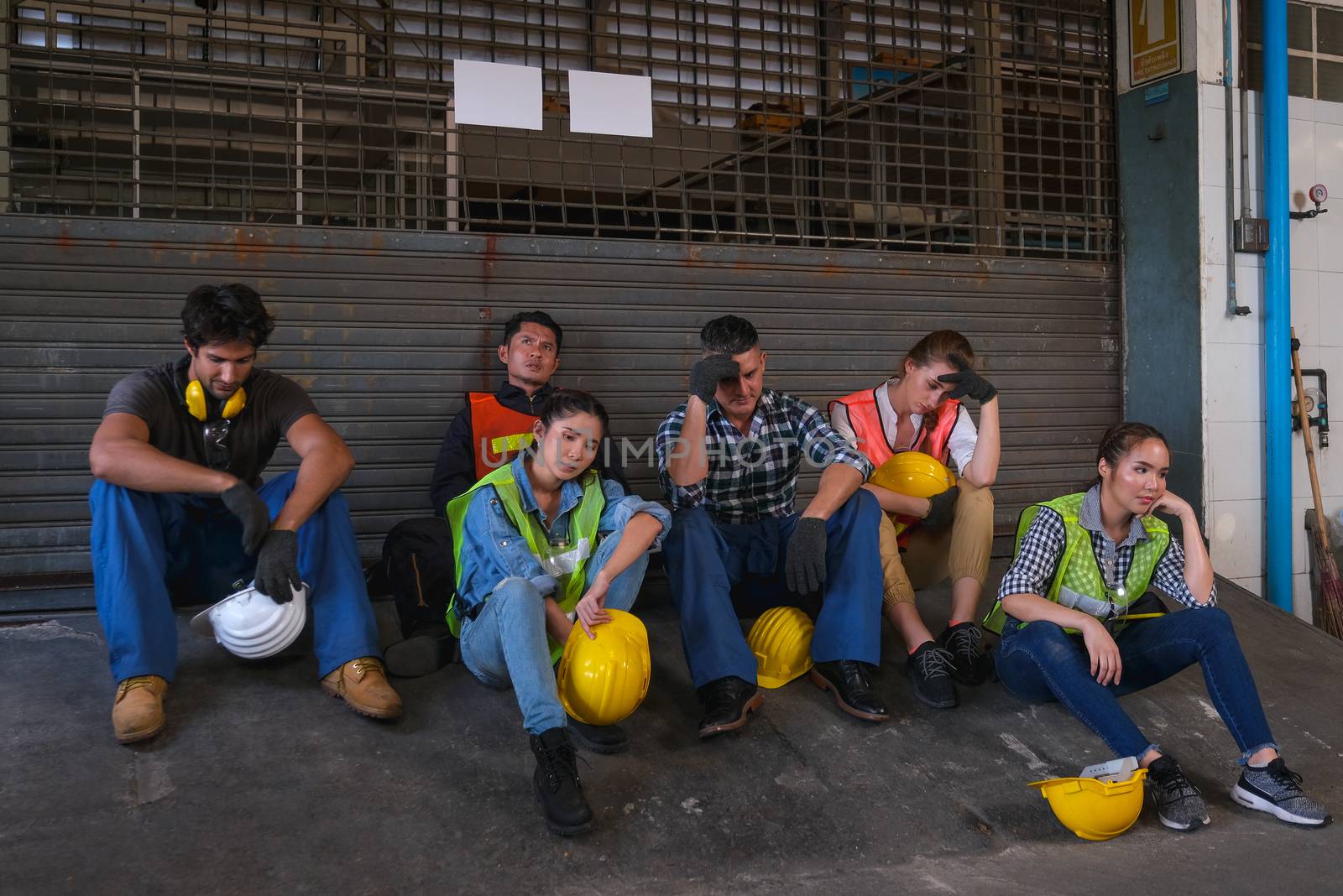 Group of technician or workers sit in front of the door of factory and end of work and they look sad.