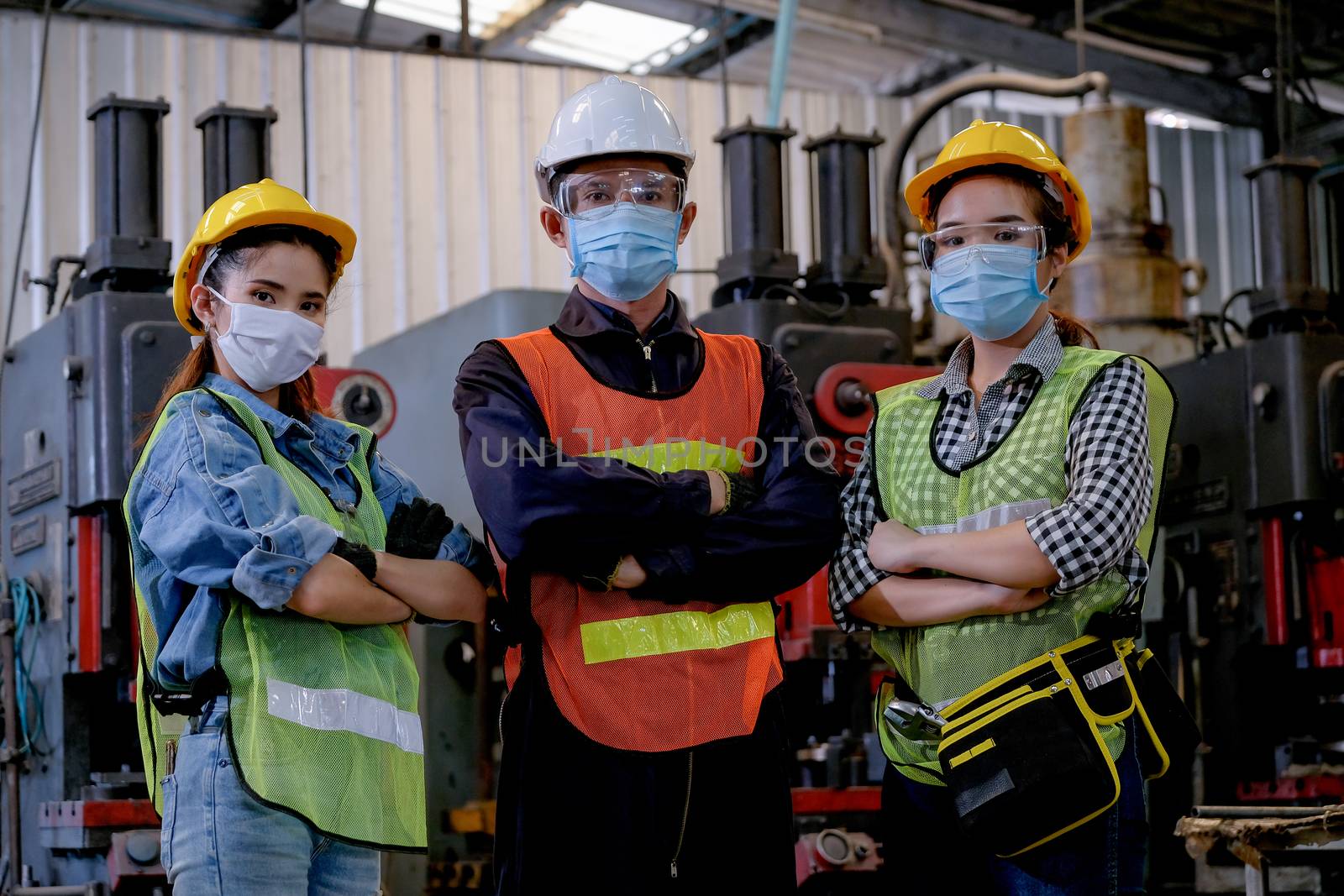 Group of man and woman workers with hygiene mask stand in confident action in the factory area.