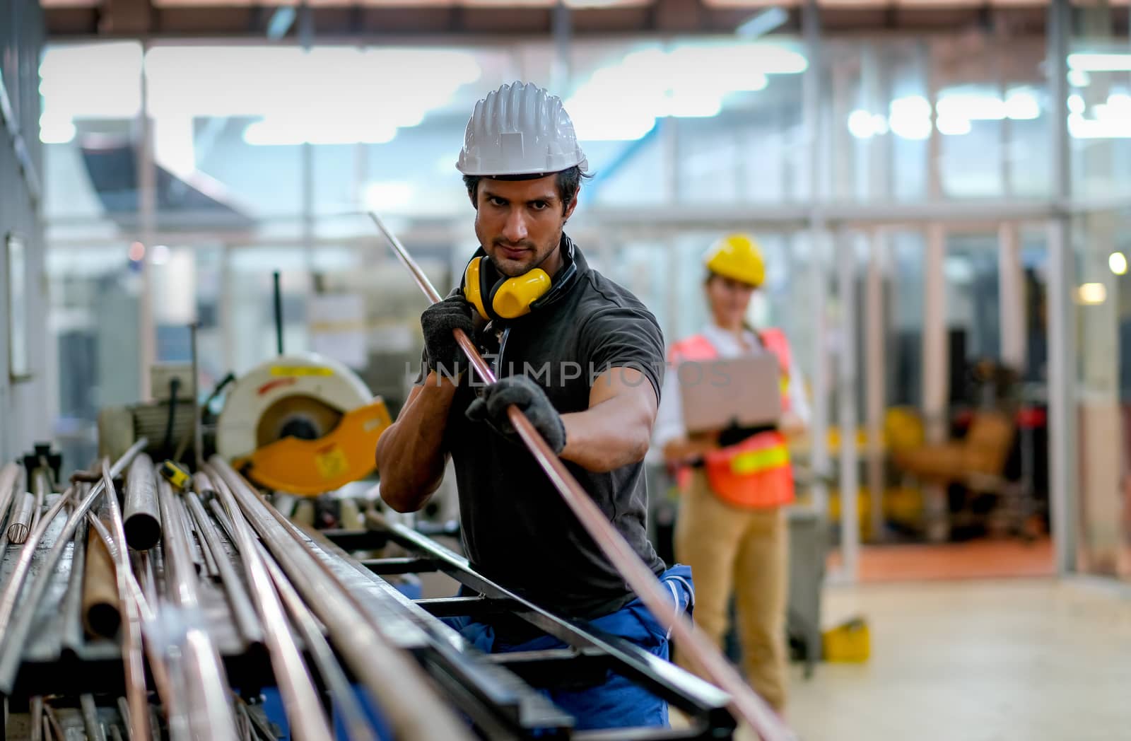 Technician or worker man hold copper tube and his co-worker hold laptop on background in factory.