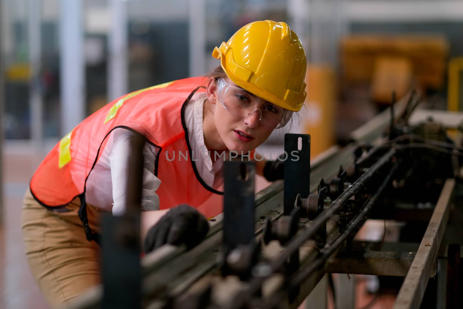 Beautiful worker or technician woman look forward through rail of some machine in factory work.
