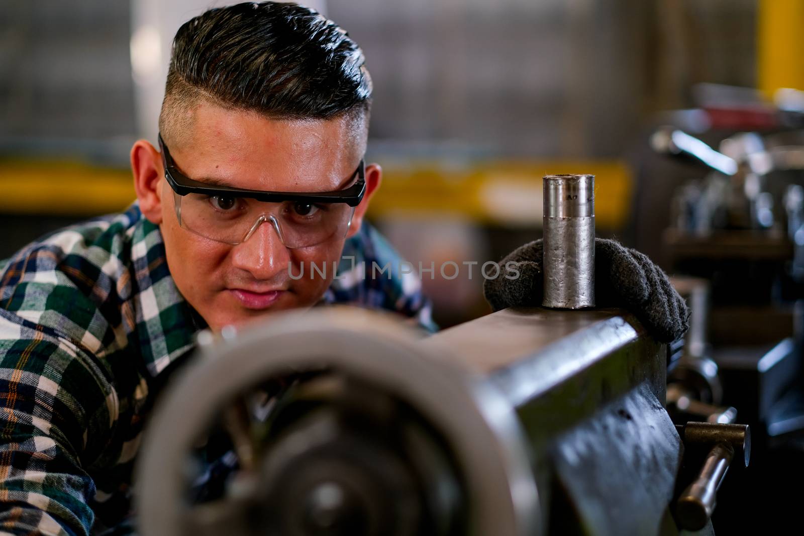 Smart technician or engineer worker man with protective eye glasses look to the machine and camera in factory workplace. Concept of good system of management to get better industrial business.