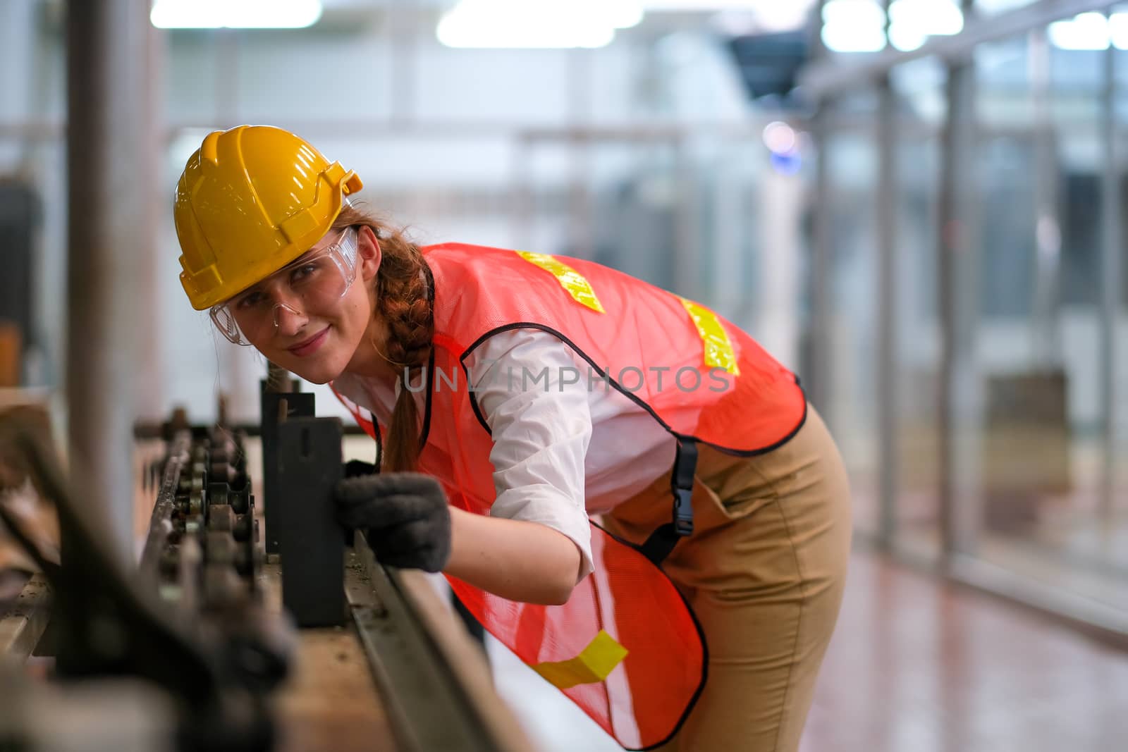 Beautiful worker or technician woman look forward through rail of some machine and also smiling with happy emotion in factory work.