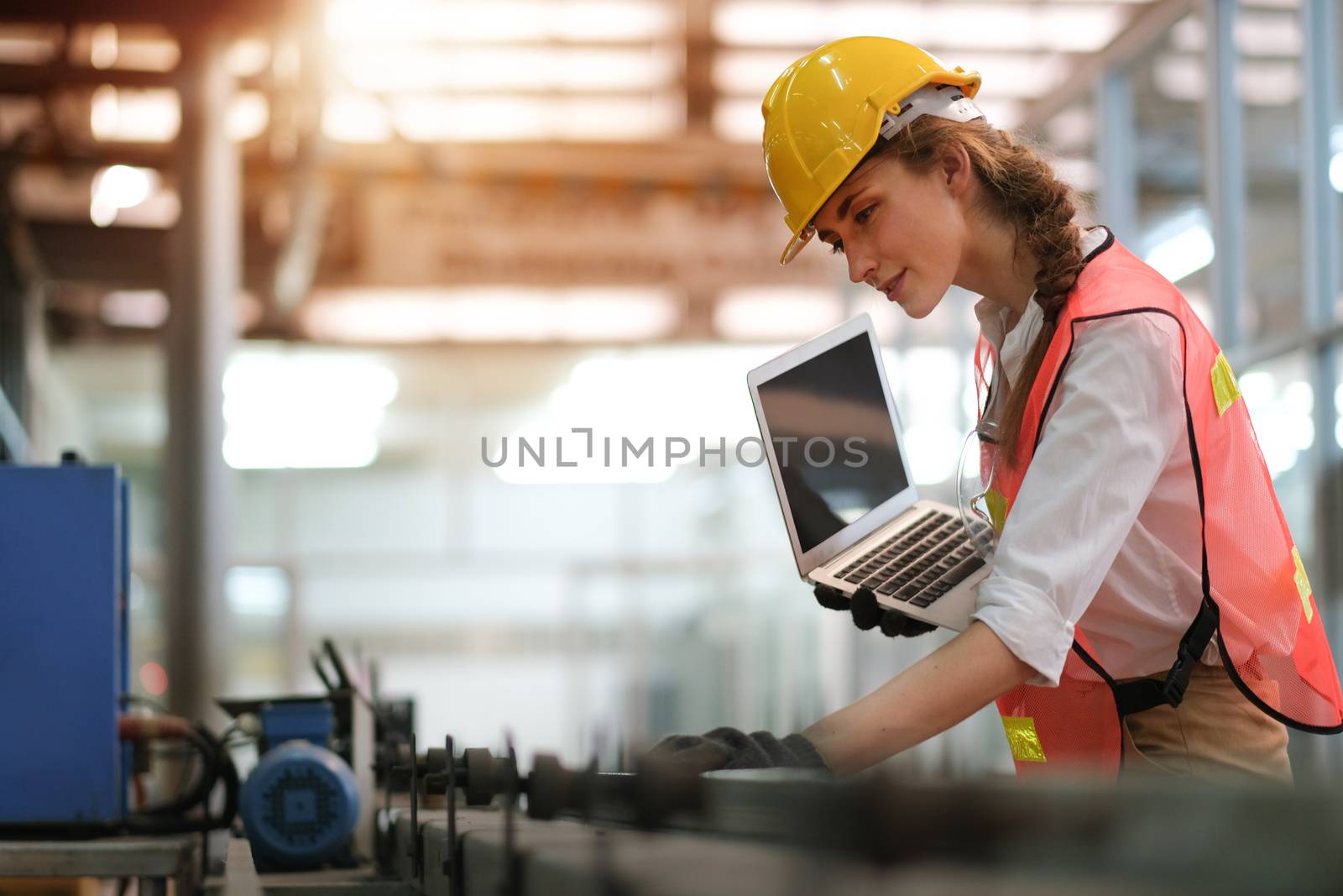 Pretty engineer or technician woman with worker uniform hold laptop computer and check status or maintenance the machine in factory with concept of happiness working for good industrial business.
