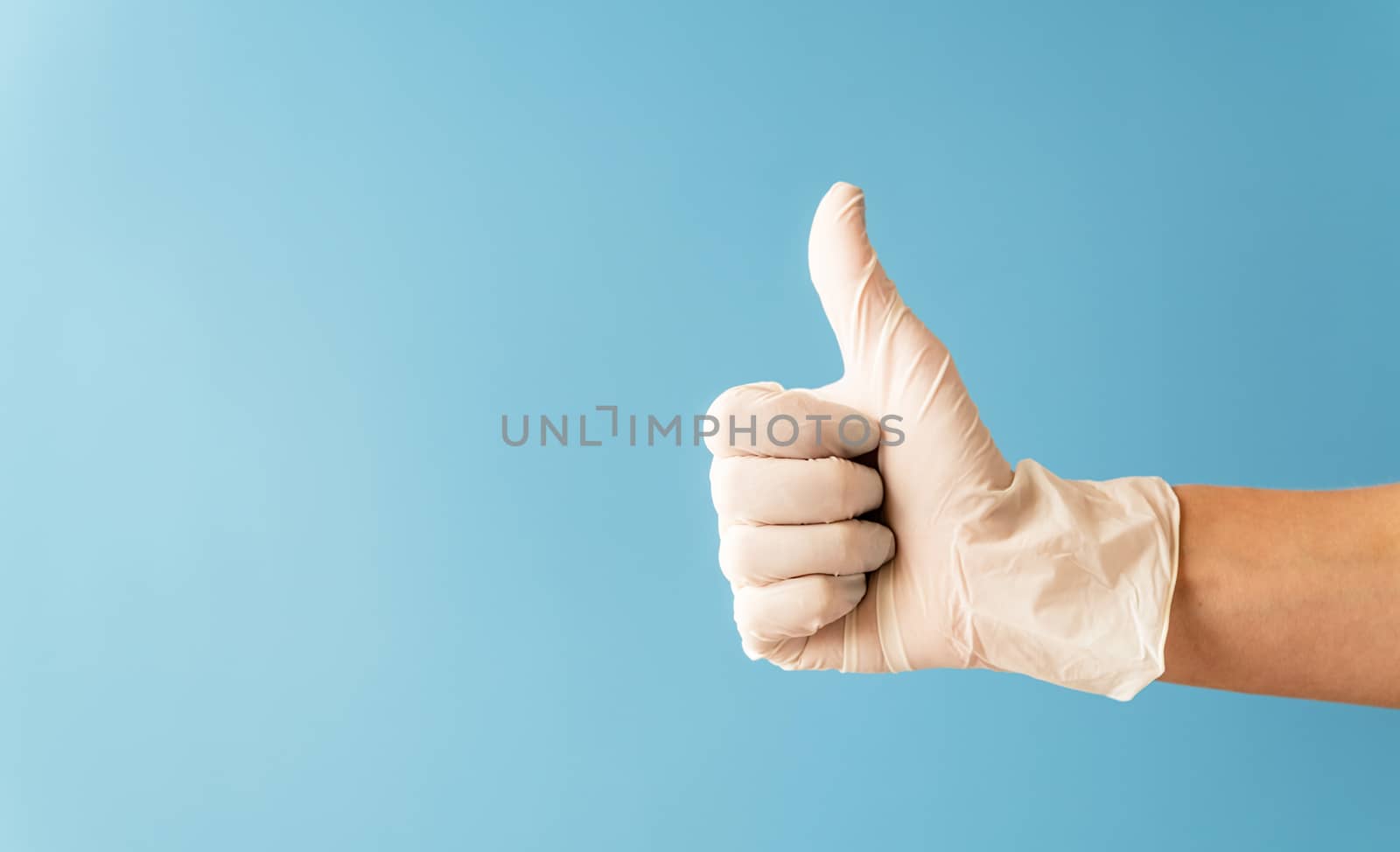 Hand wearing white rubber glove giving the thumbs up signal on blue background